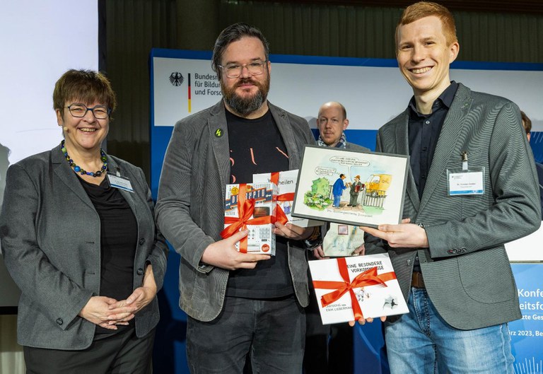 Dr.-Ing. Heike Prasse, Leiterin des BMBF-Referats „Vernetzung und Sicherheit digitaler Systeme“ ehrte Johannes Kretzschmar (Friedrich-Schiller-Universität Jena) und Dr. Thorsten Goebel (Fraunhofer IOF) als Ideengebende für die Karikatur, die zum Publikumsliebling gewählt wurde.