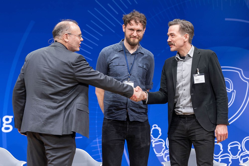 Engelbert Beyer (BMFTR) (l.) gratuliert Prof. Dr. Tim Schröder (r.) und Dr. Gregor Pieplow (m.) (beide HU Berlin) zum Sieg bei der Grand Challenge der Quantenkommunikation.