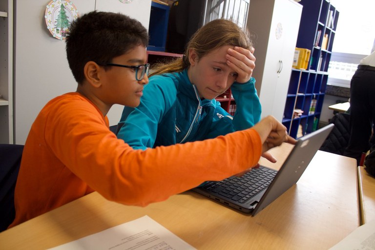 Eine Schülerinnen und ein Schüler vor einem Laptop.