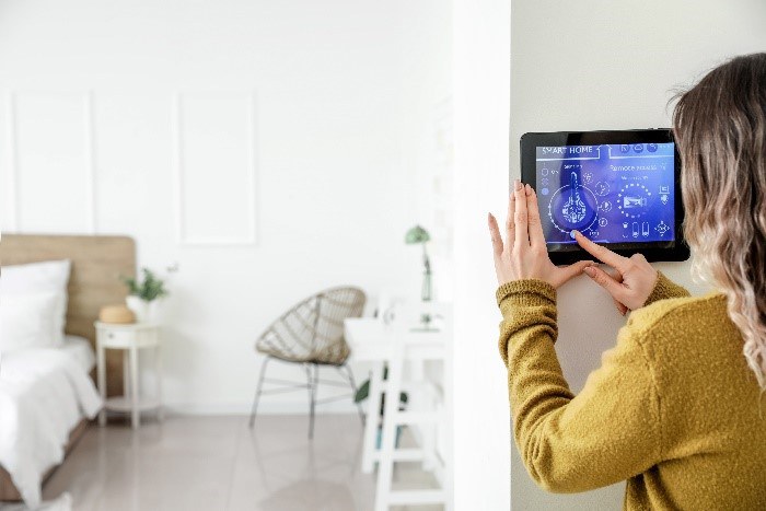 Frau hält ein Tablet zur Smarthomesteuerung. Im Hintergrund Blick ins Wohnzimmer.