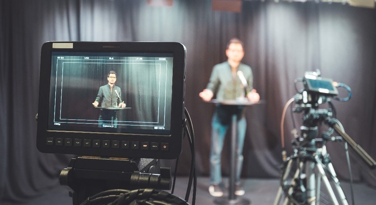 Junger Journalist in einem Fernsehaufnahmestudio, der in ein Mikrofon spricht