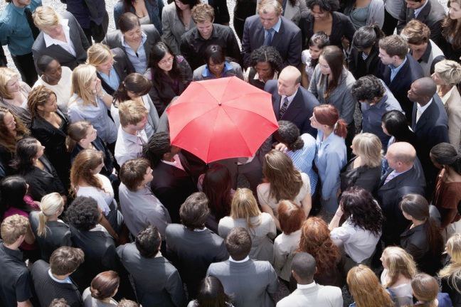 Menschenmenge mit Person, die sich unter einem roten Schirm versteckt