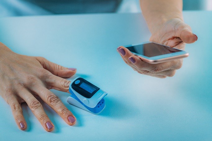 Ein Frau nutzt ein Pulsoximeter und Smartphone zur Messung der Sauerstoffsättigung