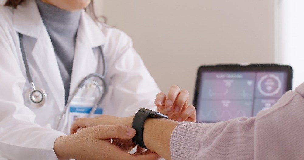 Ärztin hält den Arm einer Patientin in der Hand. Die Patientin trägt eine Fitnessuhr.